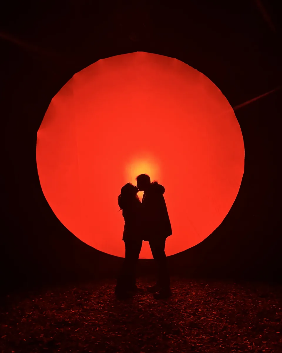 Silueta de Camila y Cristian besándose frente a un gran círculo de luz roja
